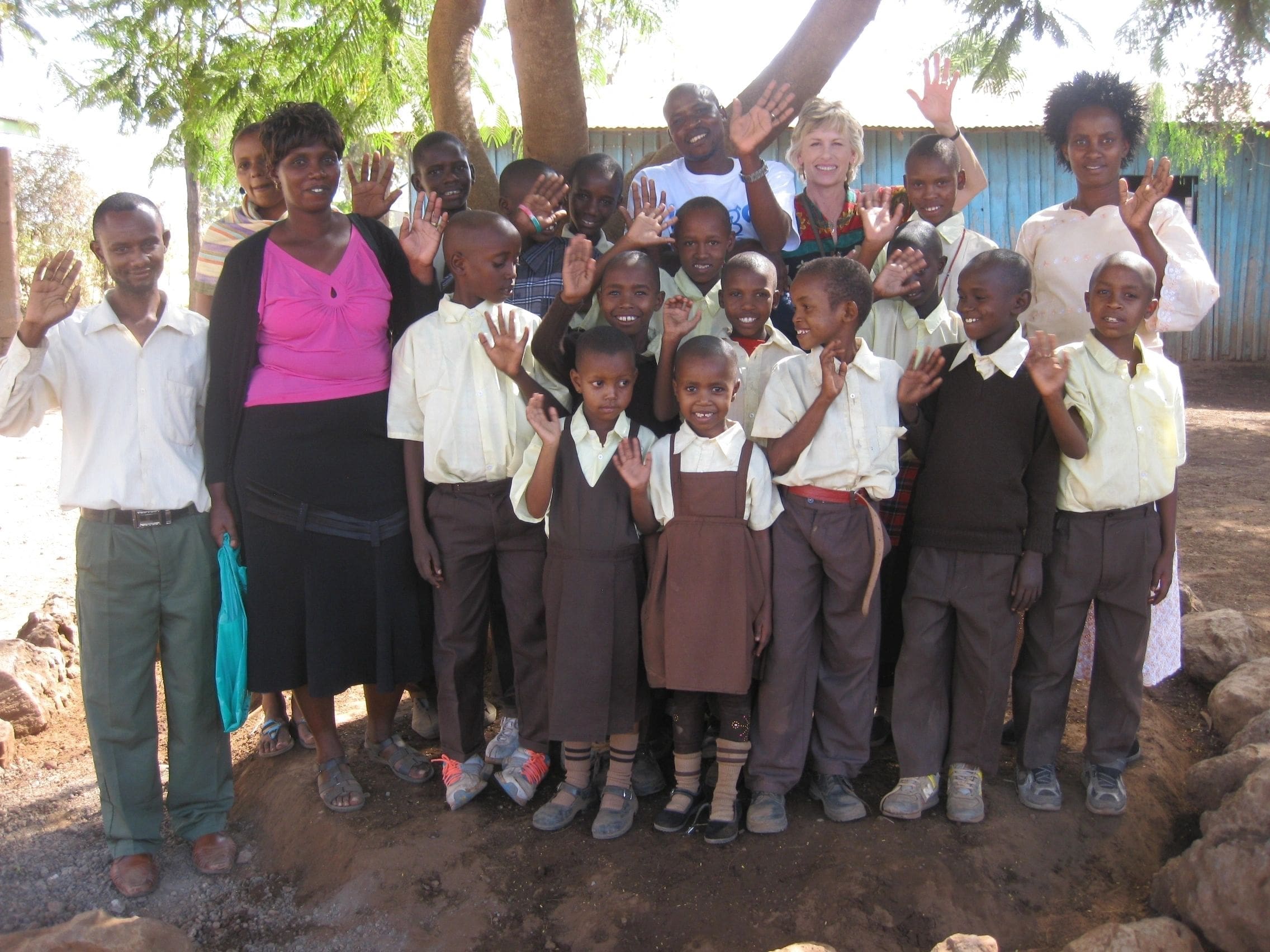 Group of children and adults posing outdoors under a tree.