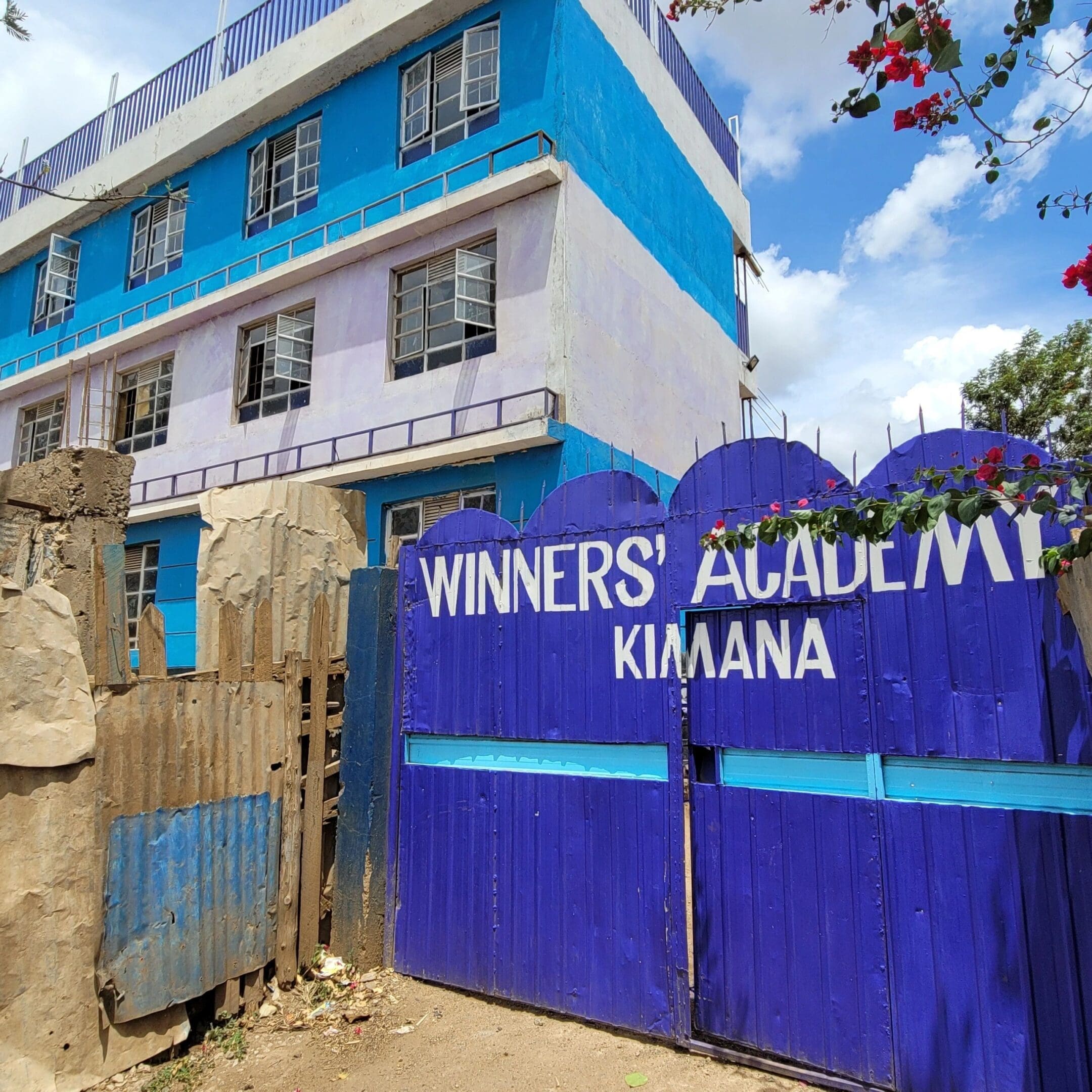 Entrance gate of Winners Academy in Kimana with a blue and white building.