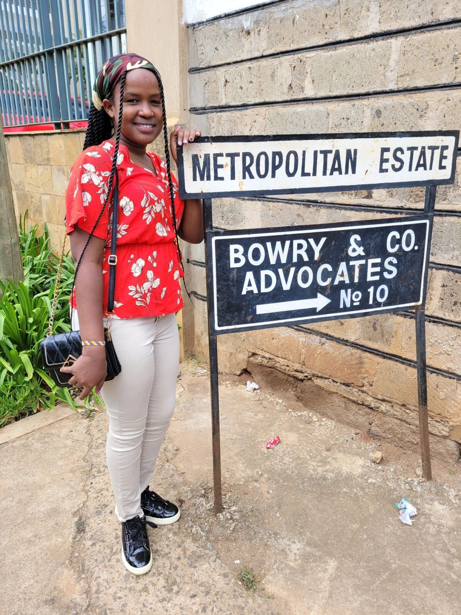 A smiling woman stands next to street signs in a casual outfit.