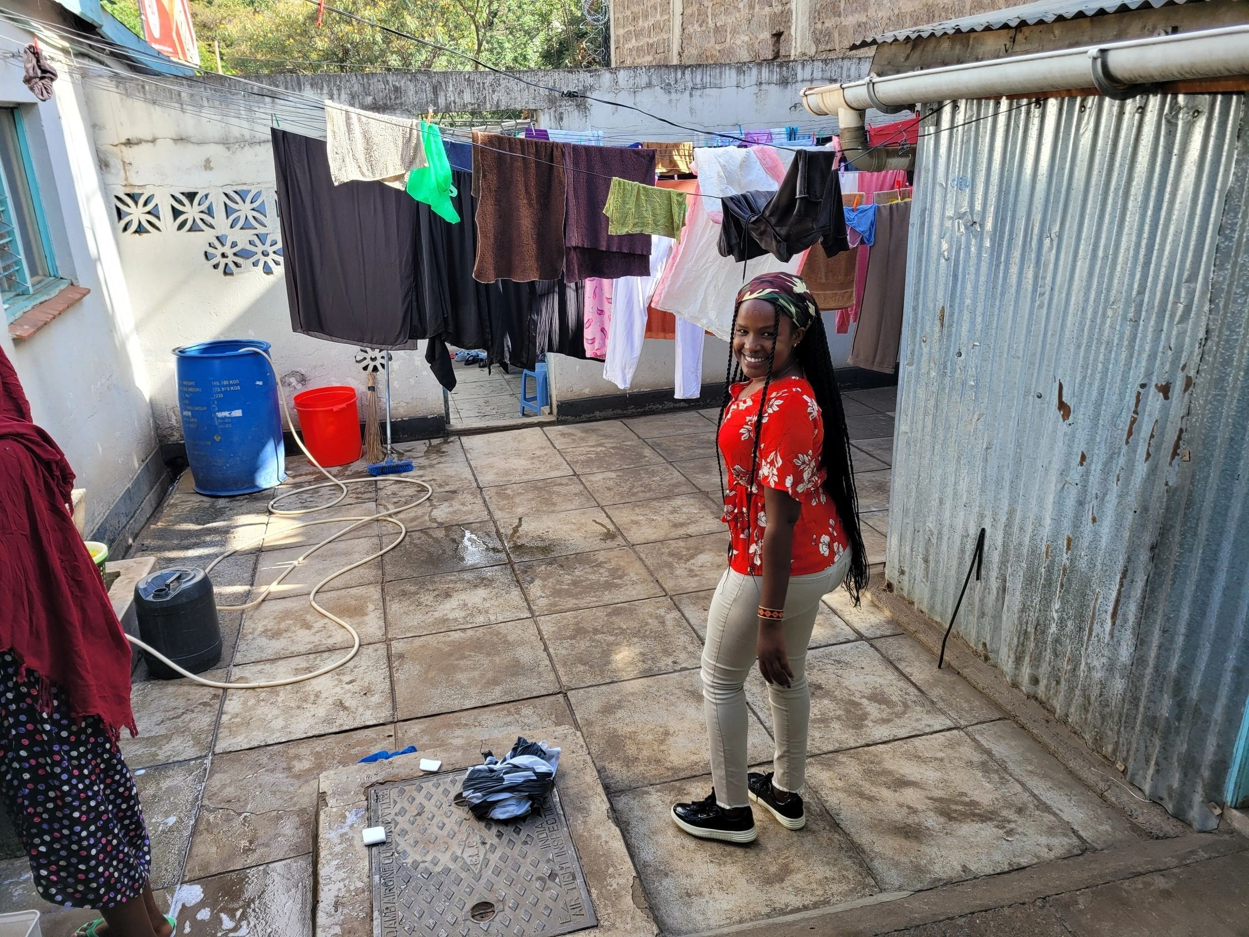 Child in red shirt standing in a cluttered backyard with clothes hanging to dry.