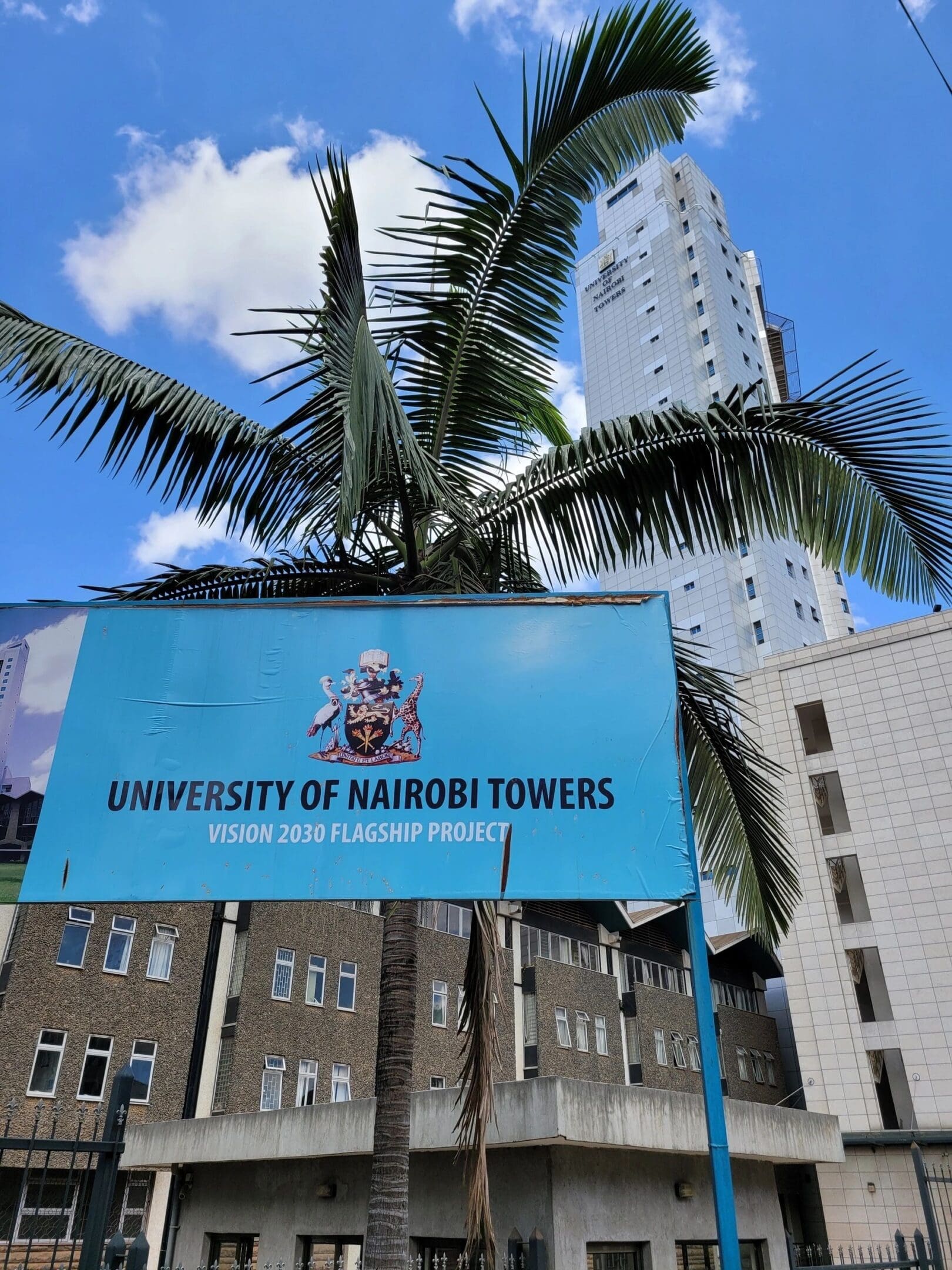The University of Nairobi Towers with palm trees against a clear blue sky.