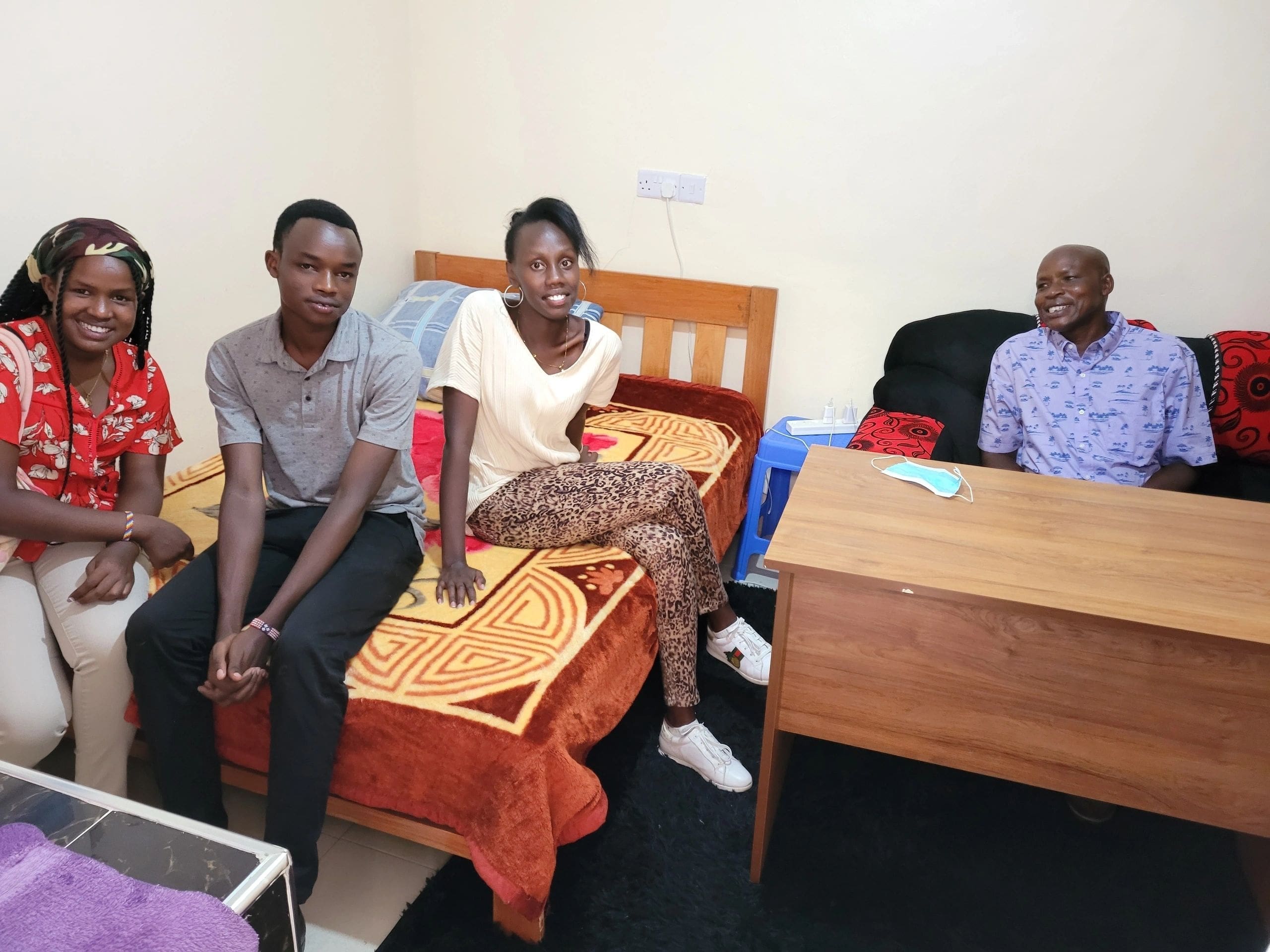 Three men sitting in a modest room with simple furniture.