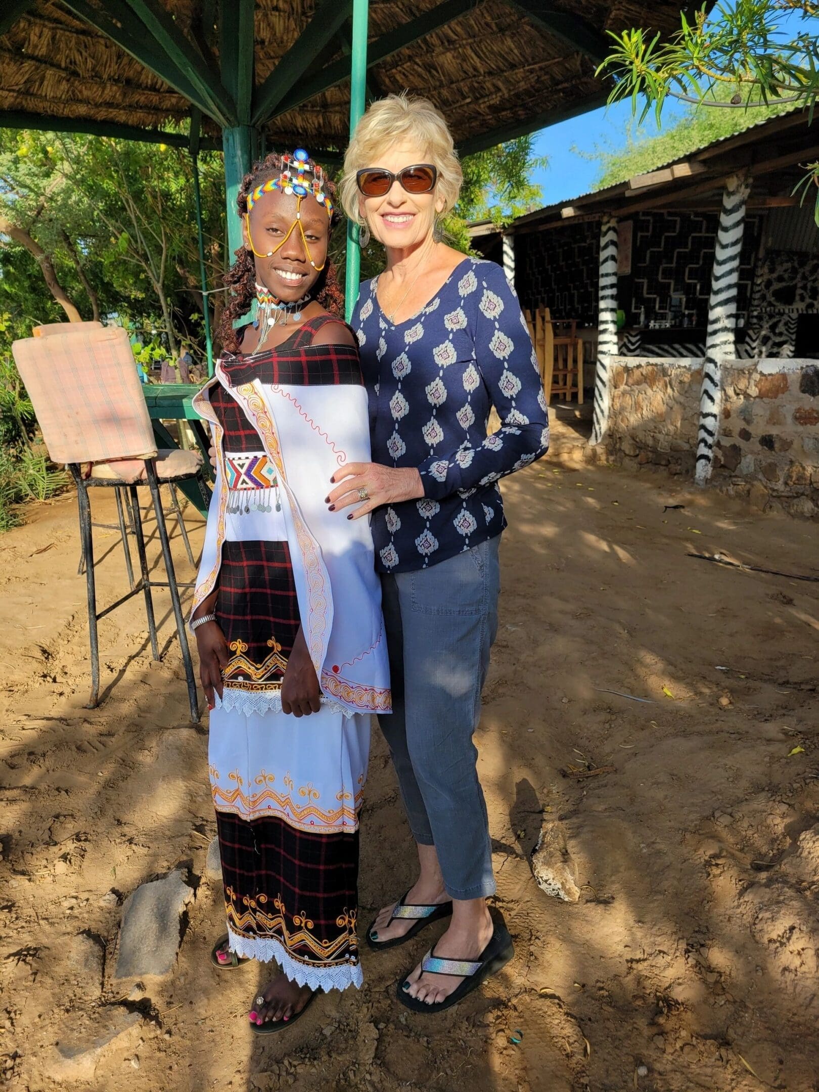 Two women smiling outdoors, holding documents in a sunny setting.