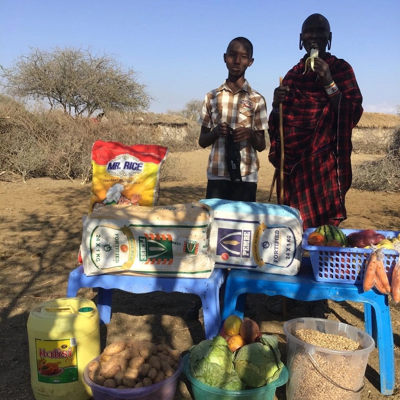 Two women standing behind a table with various food supplies outdoors.