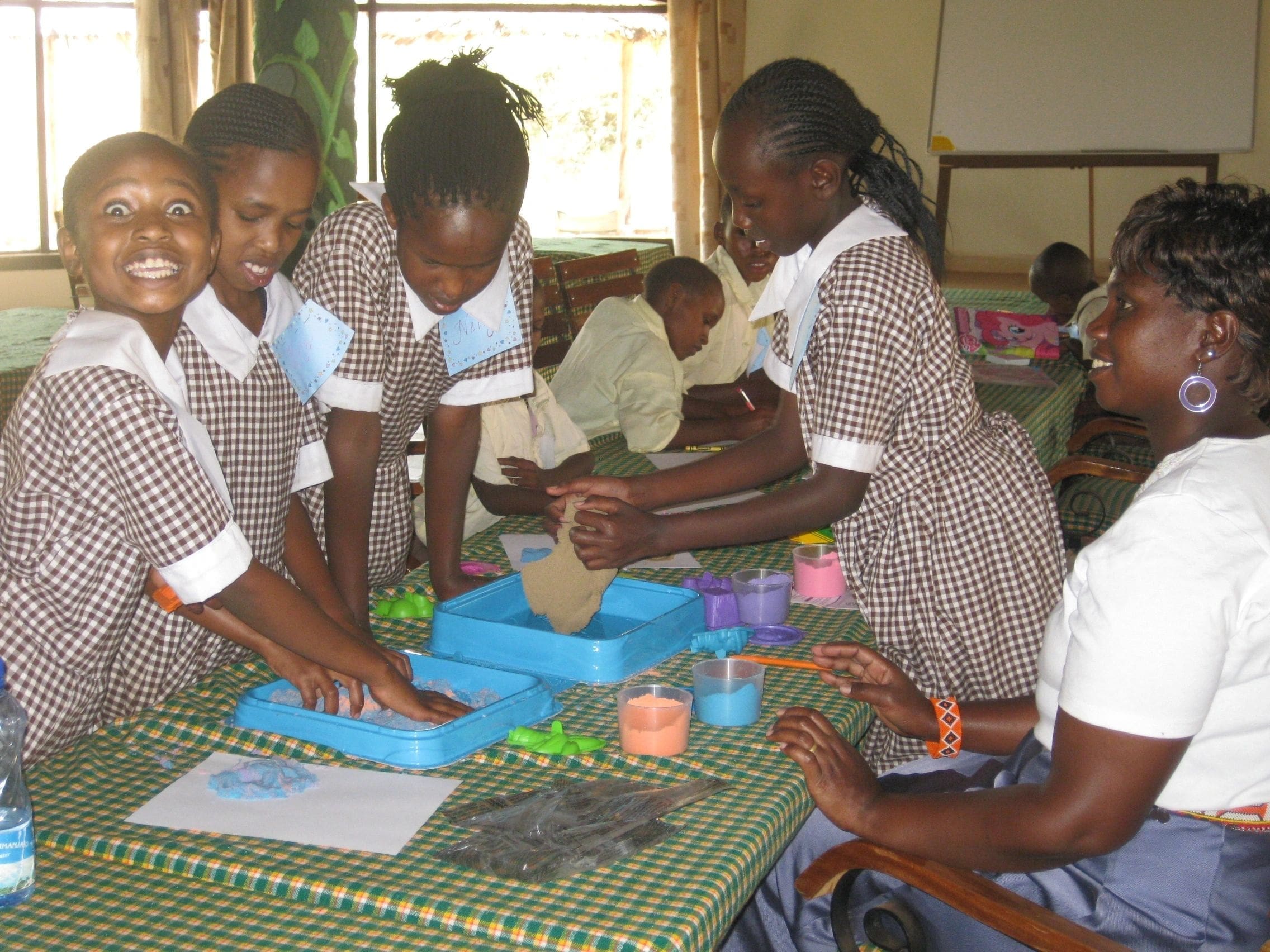 Schoolgirls in uniforms engaging in a hands-on learning activity indoors.