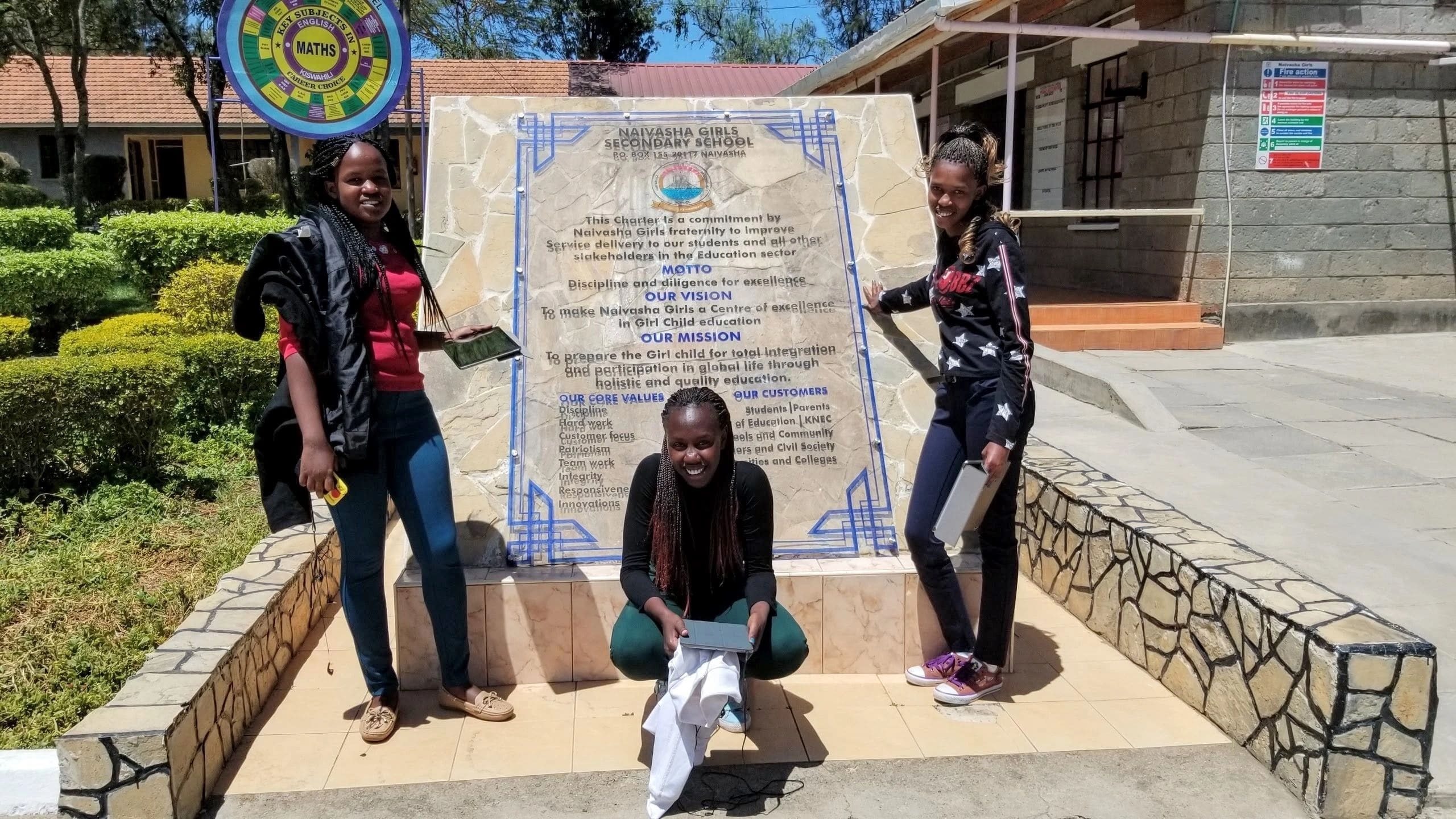 Three people posing near a large tiled plaque outdoors.