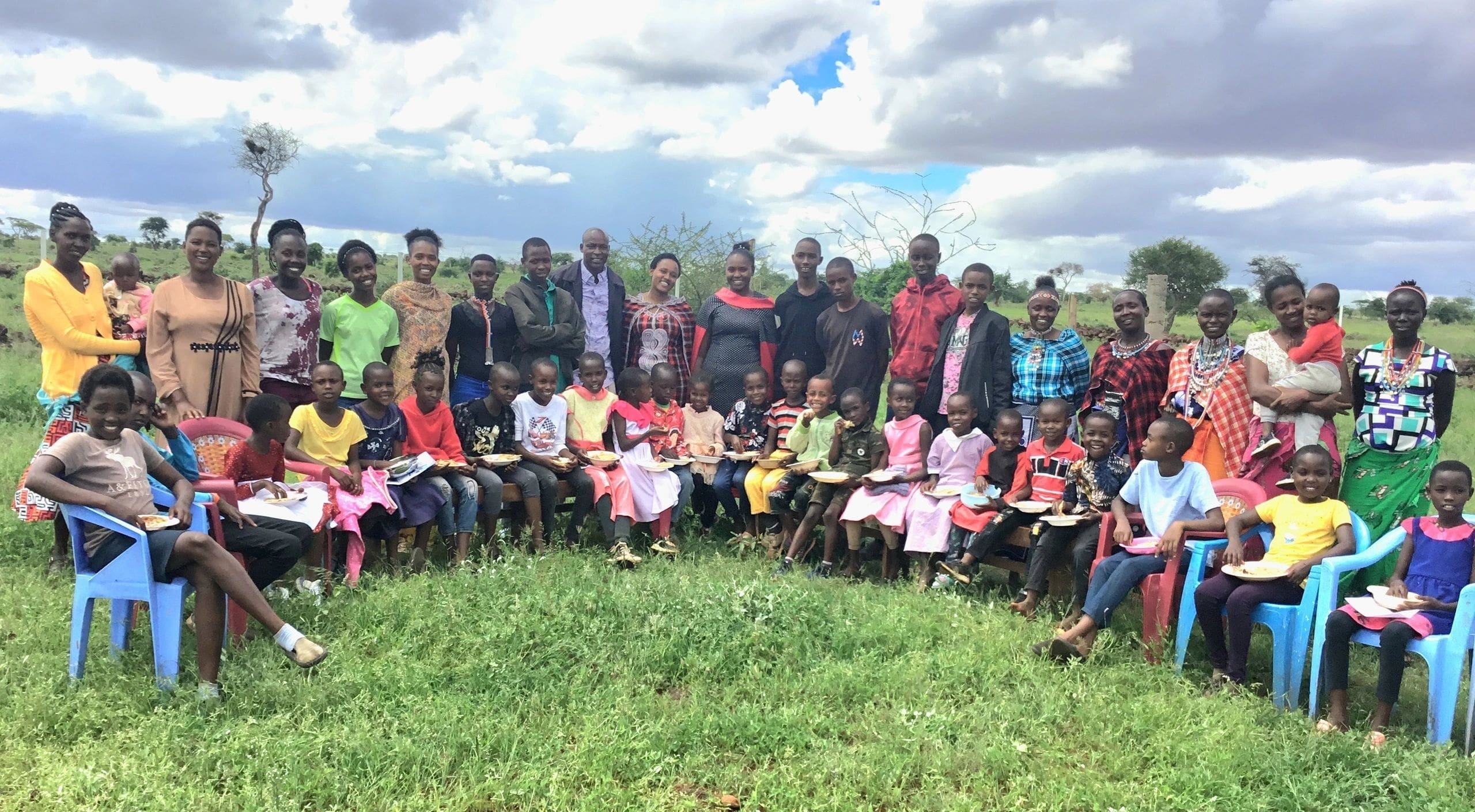 Group photo of diverse people gathered outdoors on grass under a partly cloudy sky.