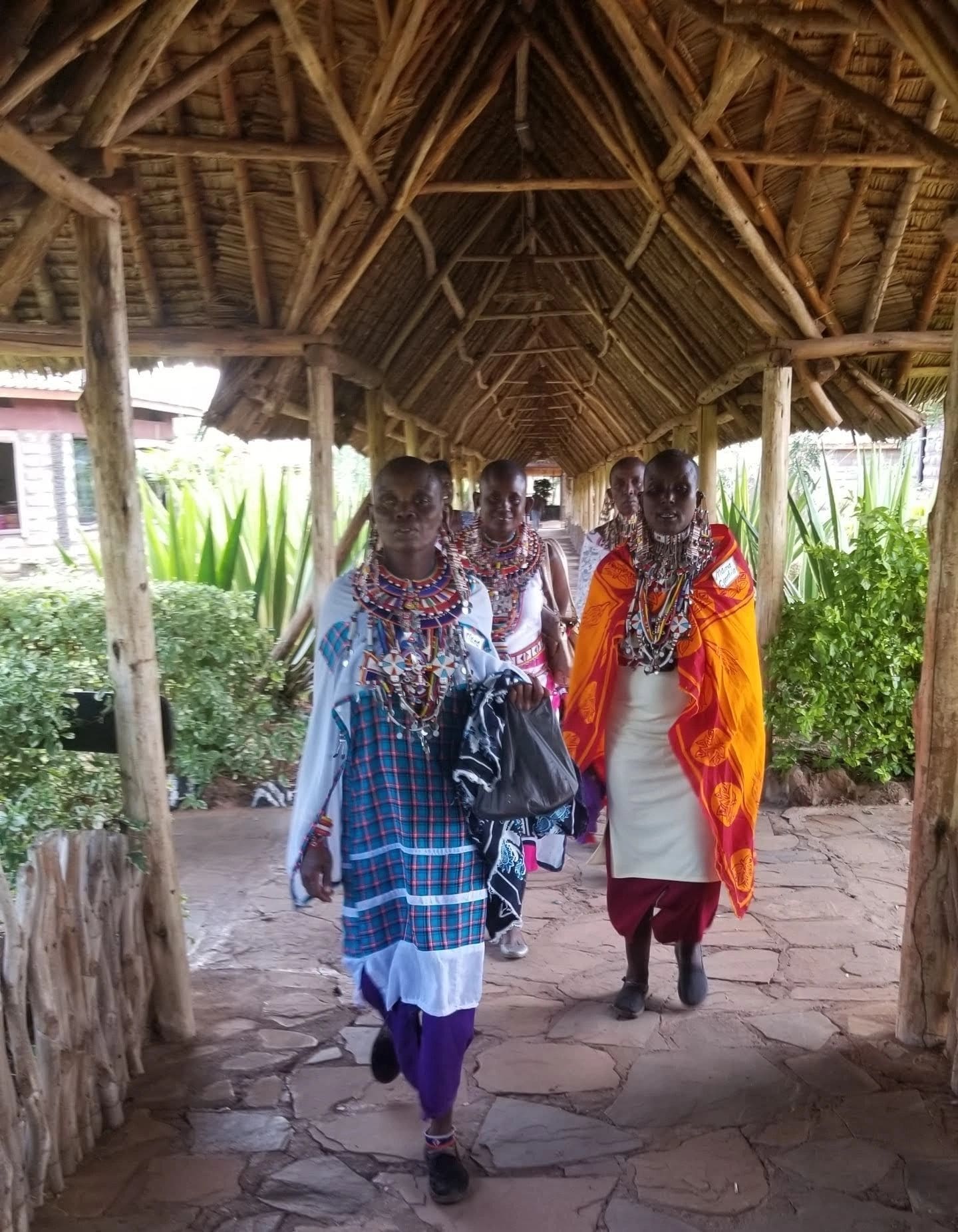 Four people in traditional Maasai clothing under a thatched roof.
