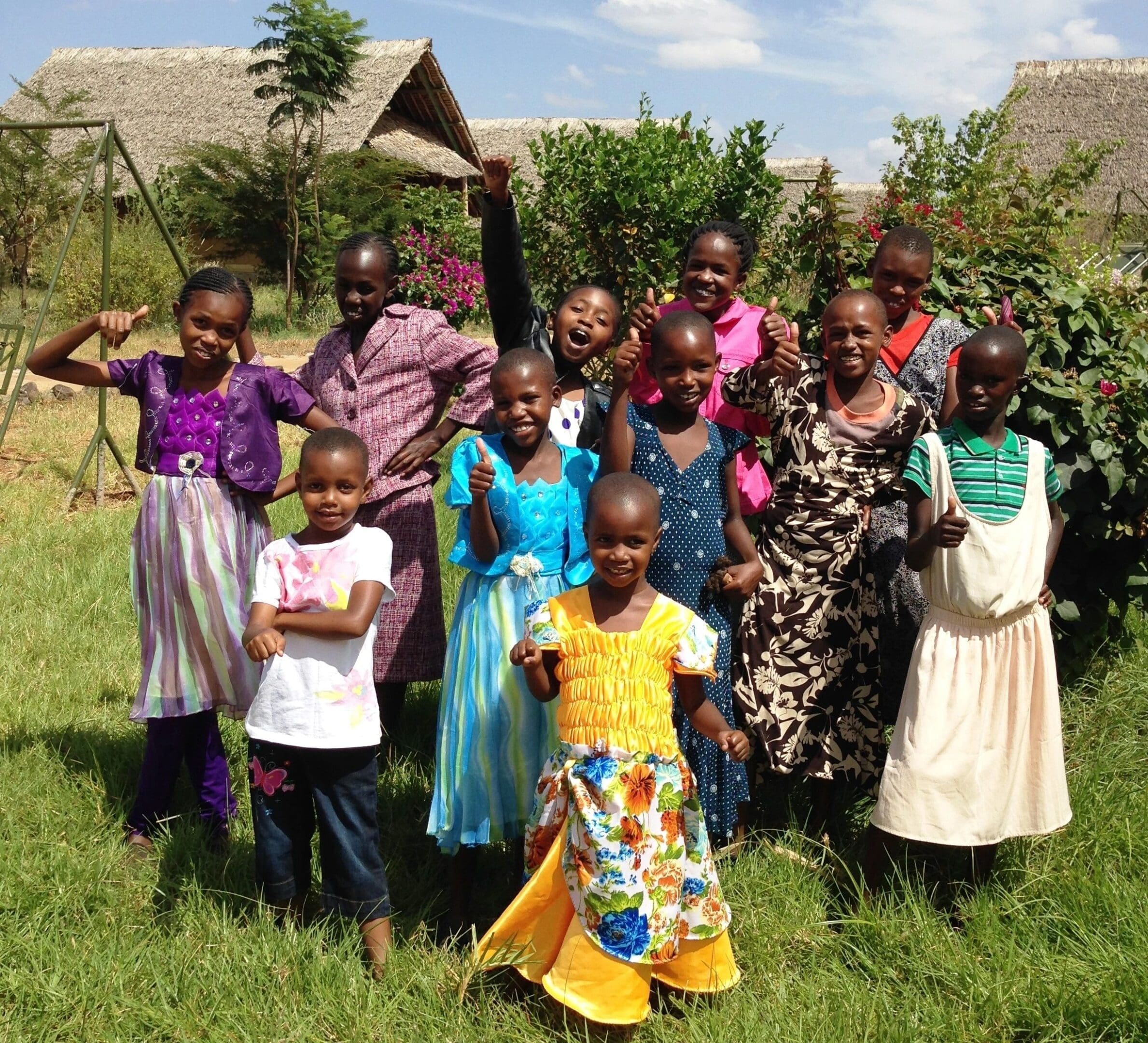 A group of children and adults smiling outdoors in colorful clothing.