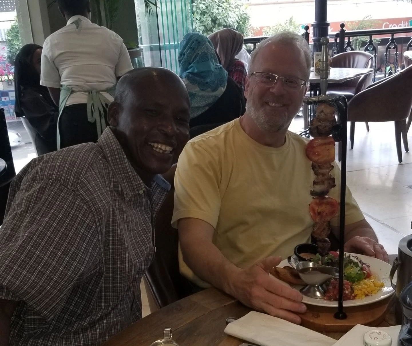 Two men smiling and enjoying a meal together at a restaurant.