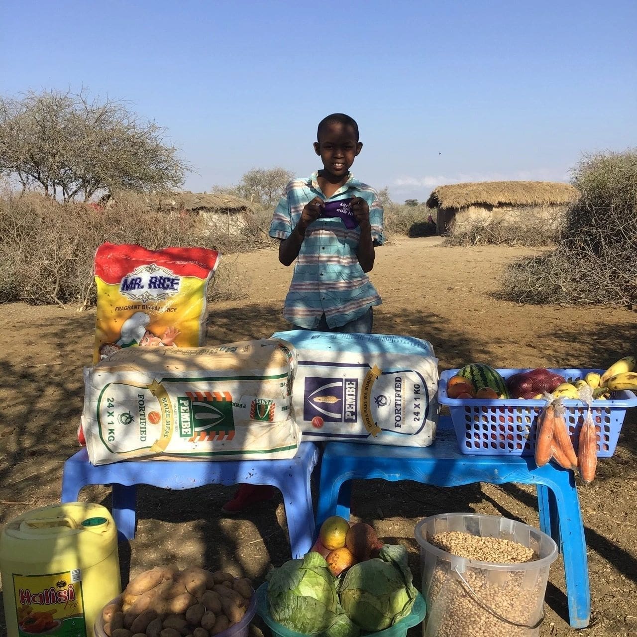 A man stands behind a table with various food items outdoors in a rural setting.