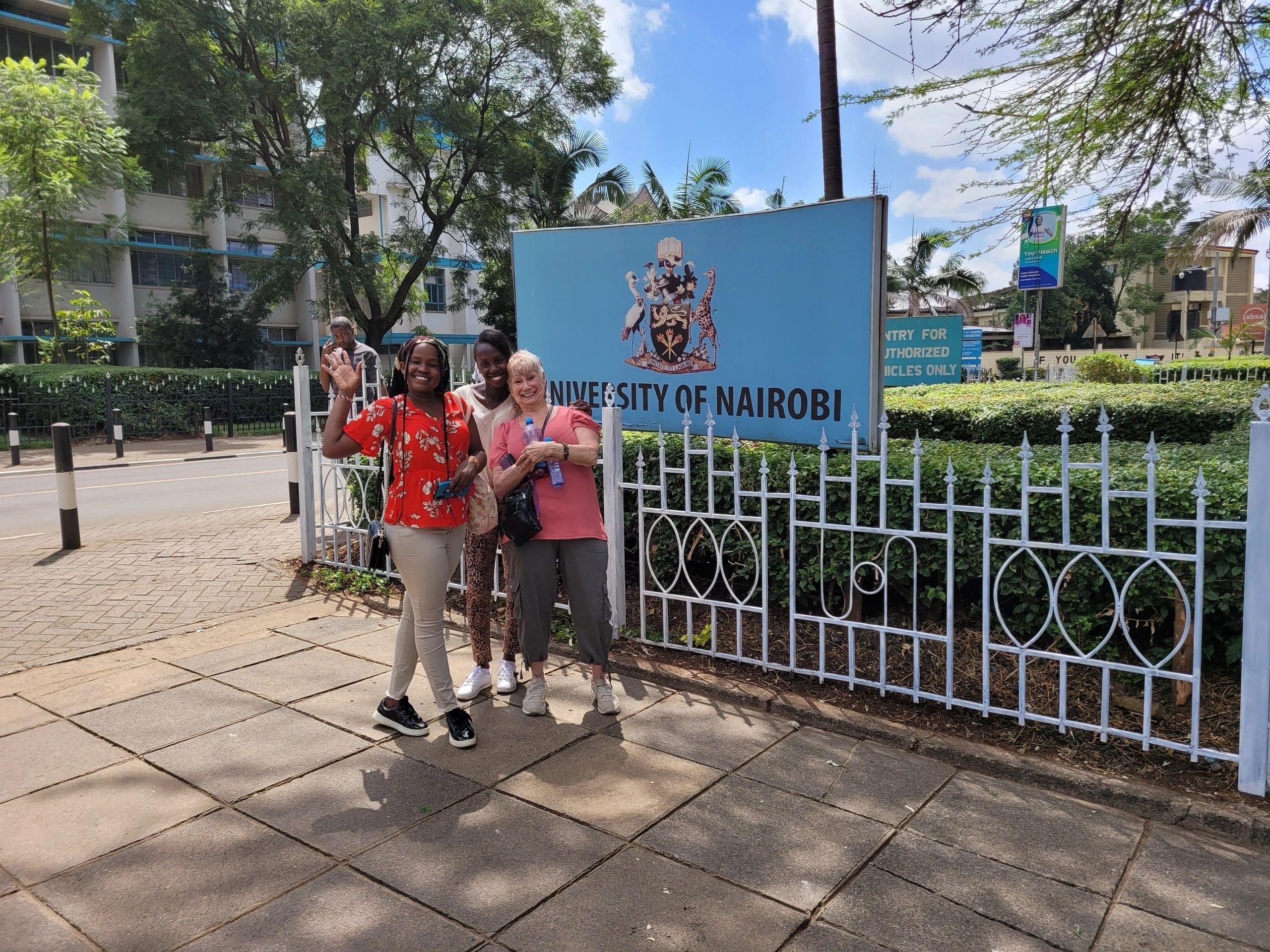 Two people posing in front of a school sign on a sunny day.