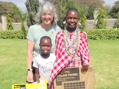A woman and two smiling children, one in traditional attire, holding a solar panel box.