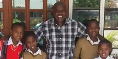 Three boys smiling together outdoors in front of a windowed building.