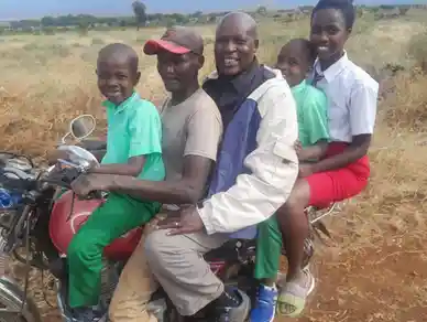 Five people riding a motorcycle on a rural dirt path.