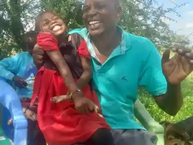 A joyful man holding a laughing child outdoors.