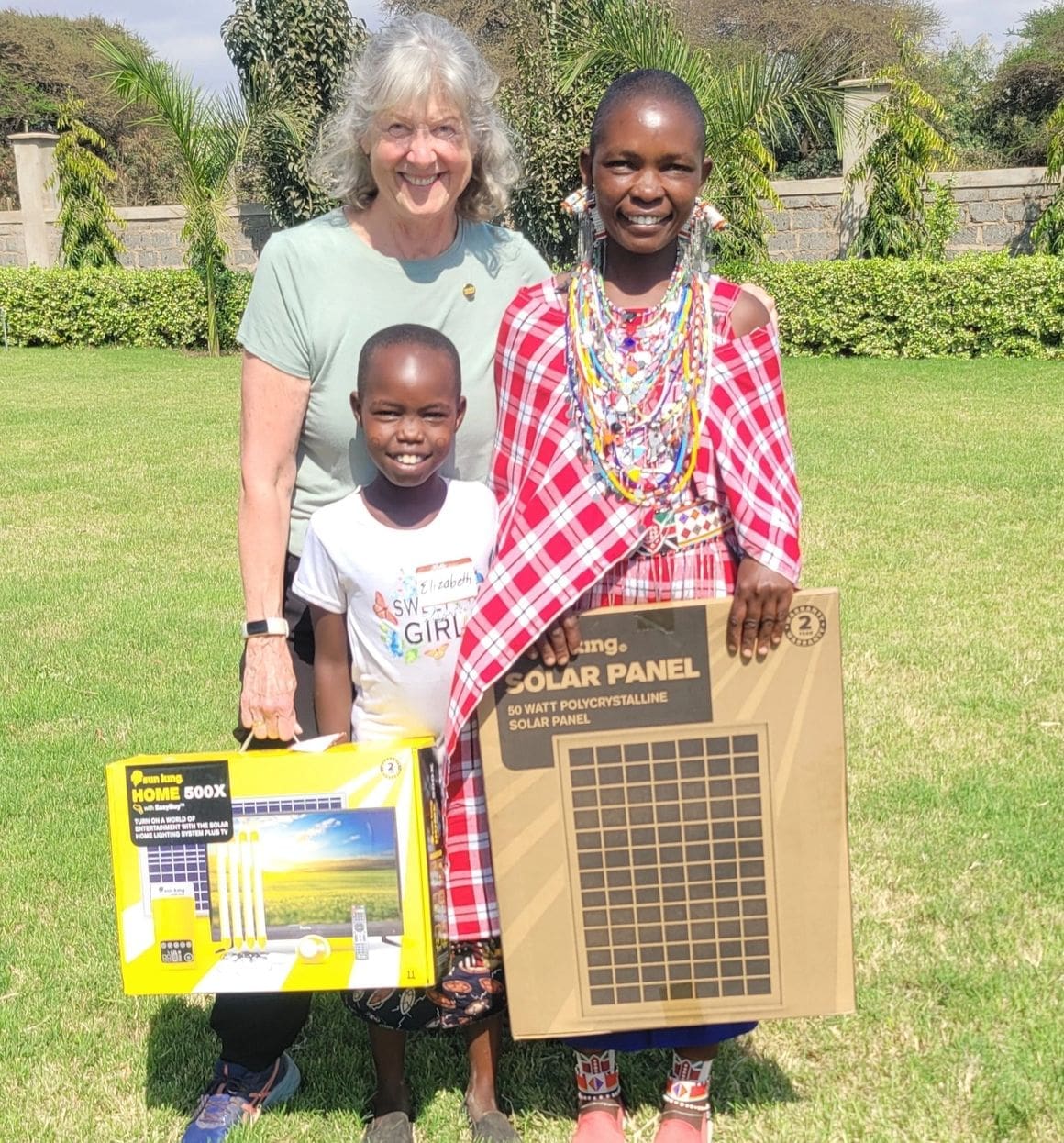 Three people smiling outdoors holding solar-related items.
