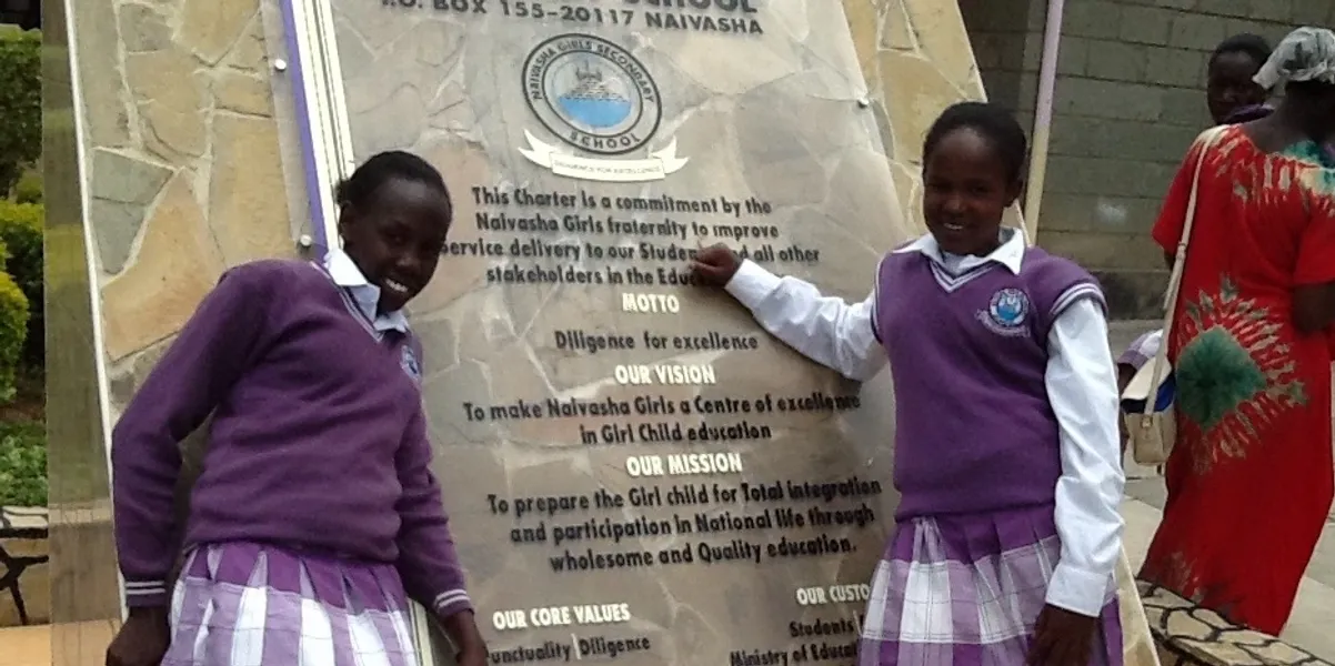 Two children in purple school uniforms smile beside an educational sign about water sanitation.