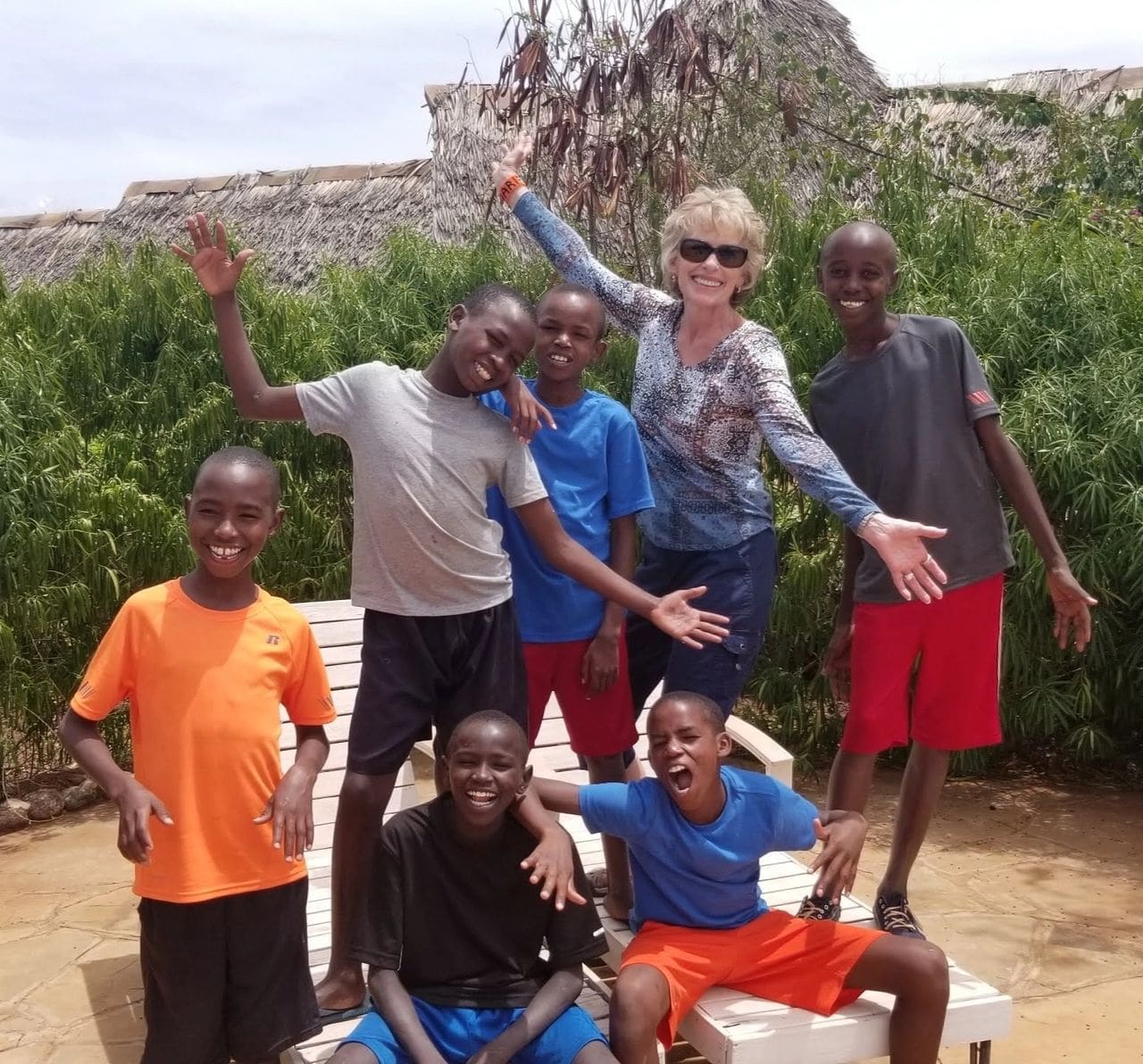 A group of seven people posing happily outdoors near bushes.
