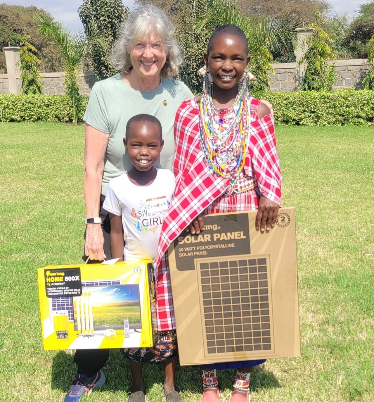Two women and a child smiling outdoors with cardboard boxes.