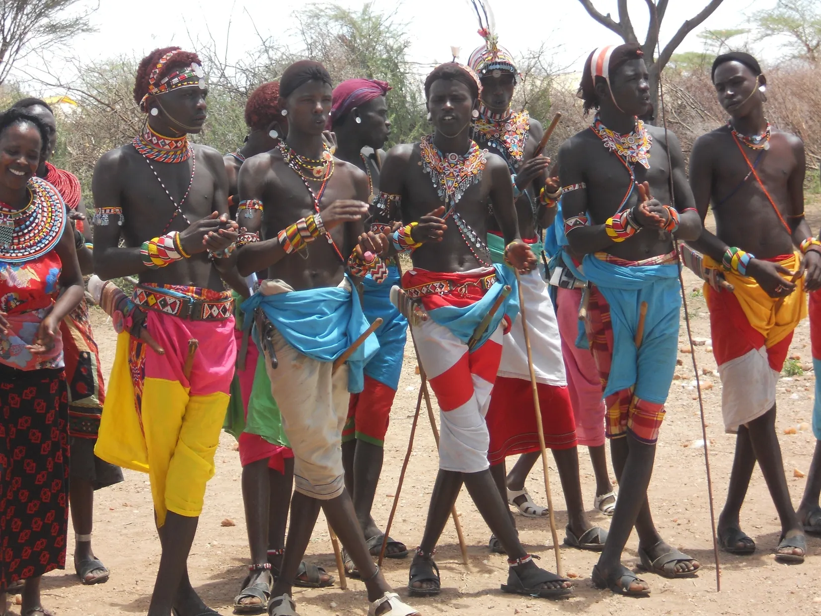 A group of traditionally dressed African women holding sticks, adorned with colorful clothing and accessories.