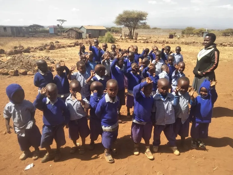 Group of children in blue uniforms posing outdoors in a rural setting.