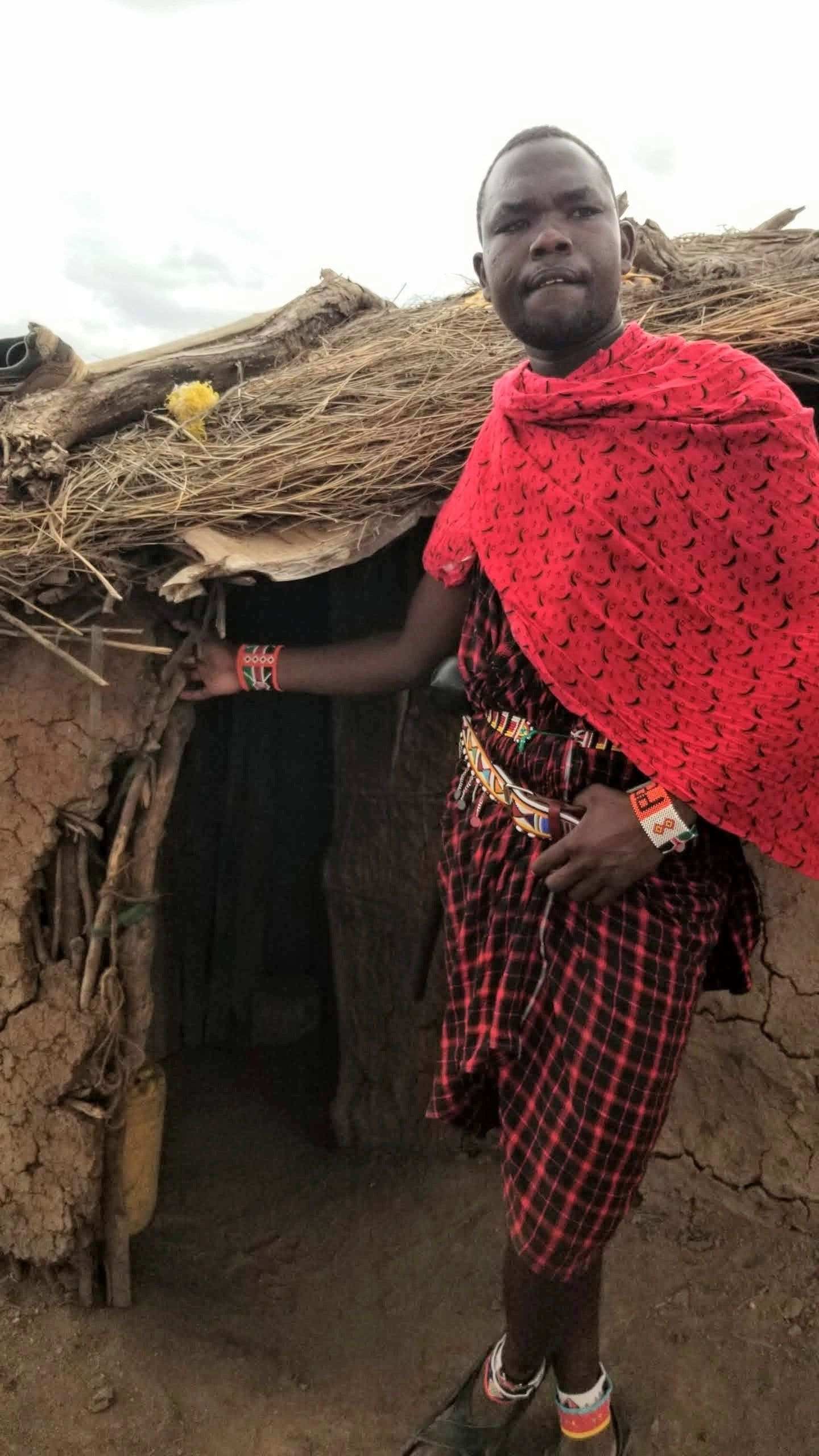 Person in traditional attire stands near a rustic thatched hut.