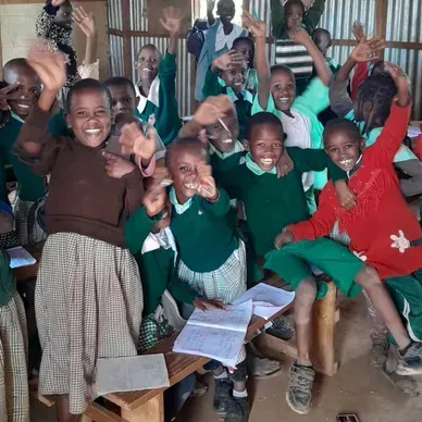 Happy children in school uniforms smiling and waving inside a classroom.