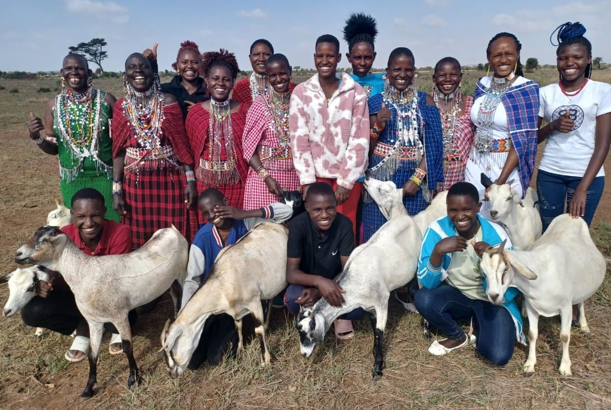 Group of people with goats posing outdoors under clear sky.