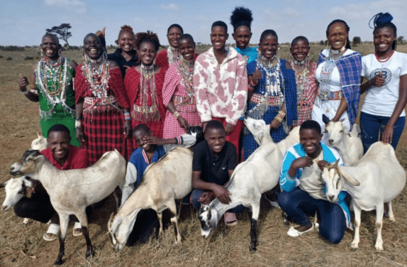 Smiling group posing with goats in grassland